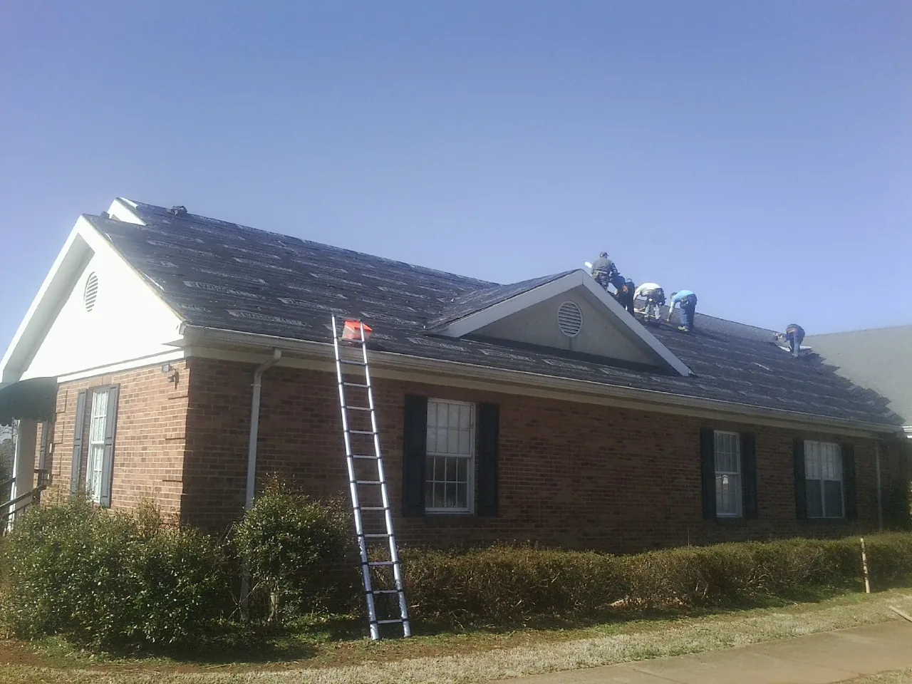 Crew tearing shingles off a brick ranch roof with a ladder set — Emergency Roof Repair work by our crew in Studio City